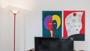 Una habitación con una lámpara de pie moderna, dos cuadros abstractos en la pared y un televisor sobre un soporte de madera.