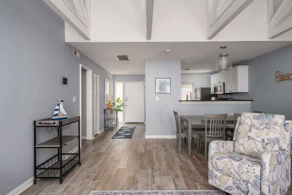 Una sala de estar moderna con un sofá, una mesa de comedor con sillas y una zona de cocina con armarios y una lámpara colgante.