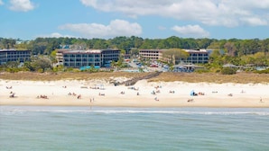 Um hotel à beira-mar com vários edifícios, uma praia de areia e um fundo coberto por floresta.