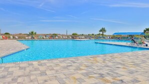 Piscina com deck ladrilhado e cadeiras de sol.