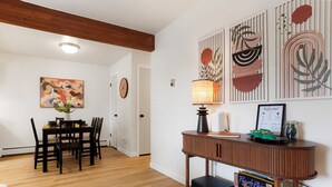 A dining area with a wooden table and chairs, a vase of flowers, and a wall with abstract art and a lamp. - Boulder Retreat w/ Pool & Mountain Views (Boulder)