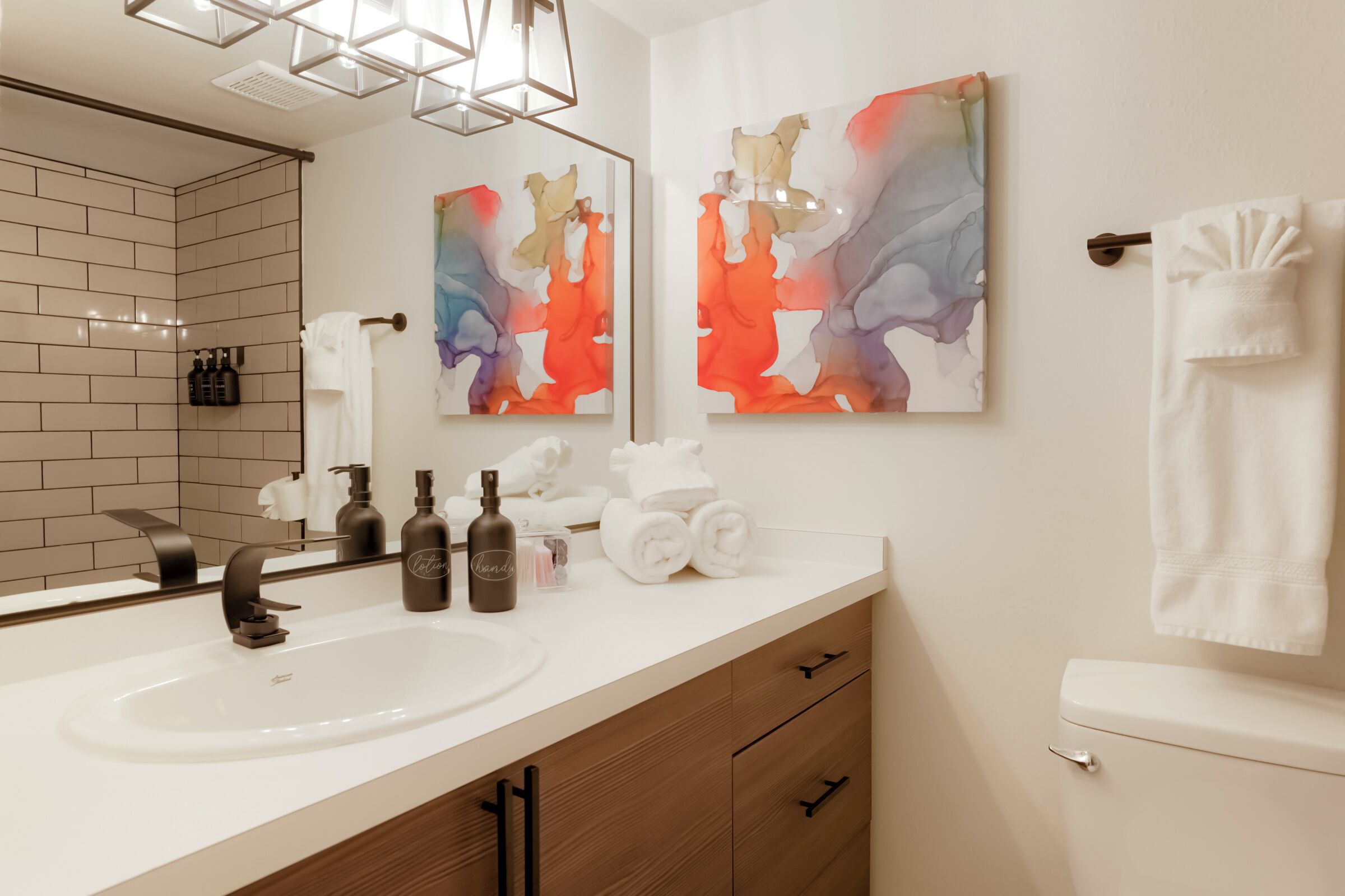 A modern bathroom with a white sink, wooden cabinets, and two abstract paintings.