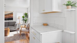 A modern kitchen with white cabinetry, a marble countertop, and a wooden chair.