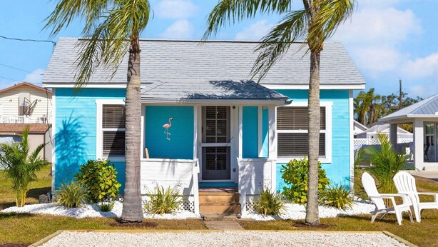 A two-story house with a blue exterior and a white porch. There are two palm trees in front of the house.
