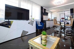 Un salon moderne avec un téléviseur à écran plat, un fauteuil bleu et une table basse agrémentée d’un vase décoratif.