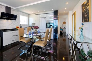 A modern kitchen with a dining area, a flat-screen TV mounted above the counter, and a glass dining table with chairs. - Apartment 'La Reina' with Sea View, Wi-Fi and Air Conditioning (Calpe)