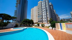 A swimming pool surrounded by high-rise buildings, a clear sky, and a sign with information. - Apartment 'La Reina' with Sea View, Wi-Fi and Air Conditioning (Calpe)