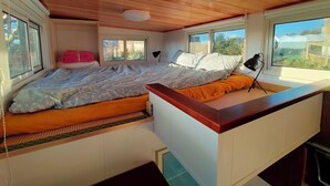 A compact bedroom with a bed, a small desk, and a window providing a view of the outdoors. - The Cyberhut (Underwood)