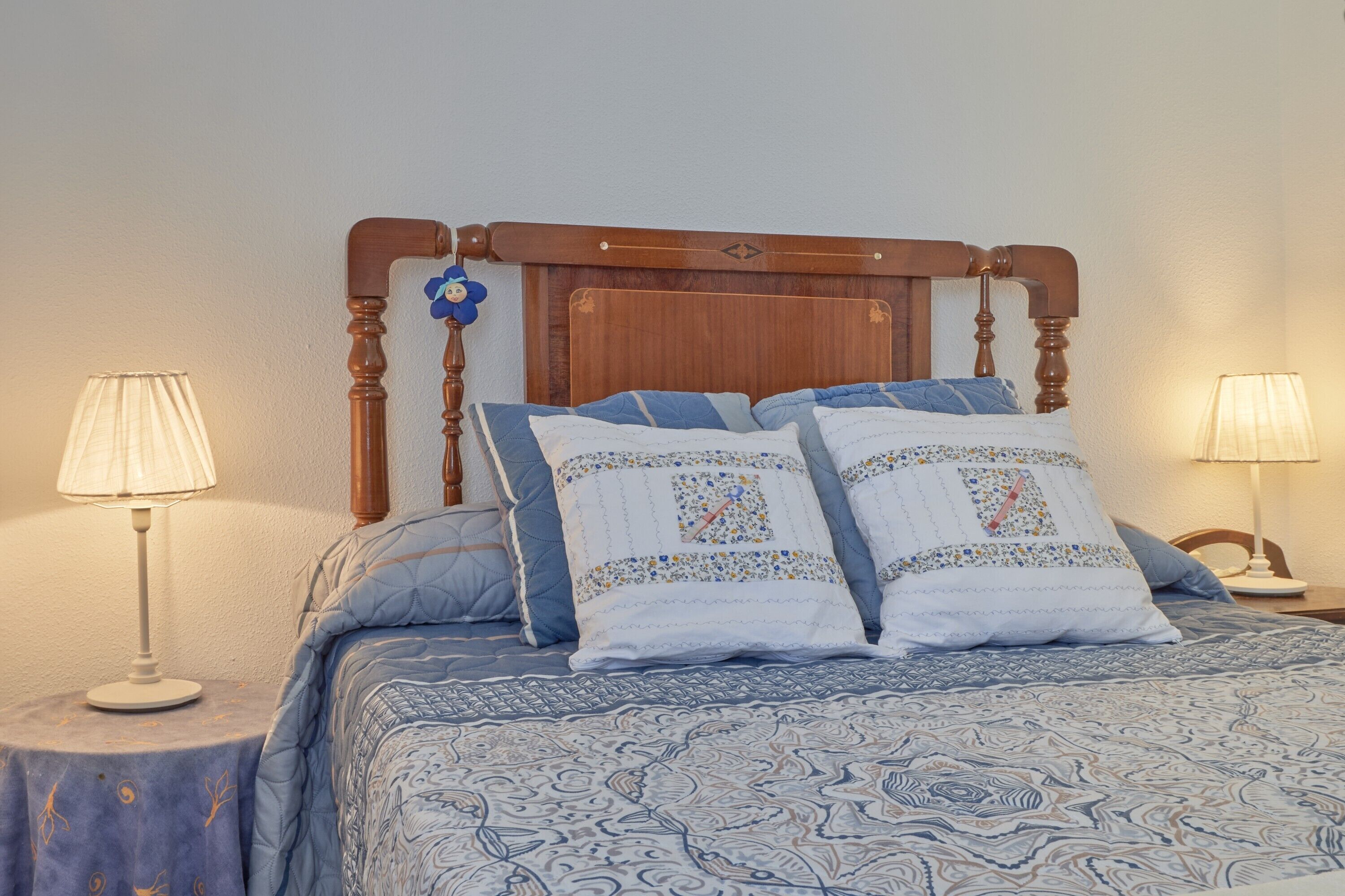 Un lit avec une tête de lit en bois, deux lampes de chevet et une couvre-lit à motifs.