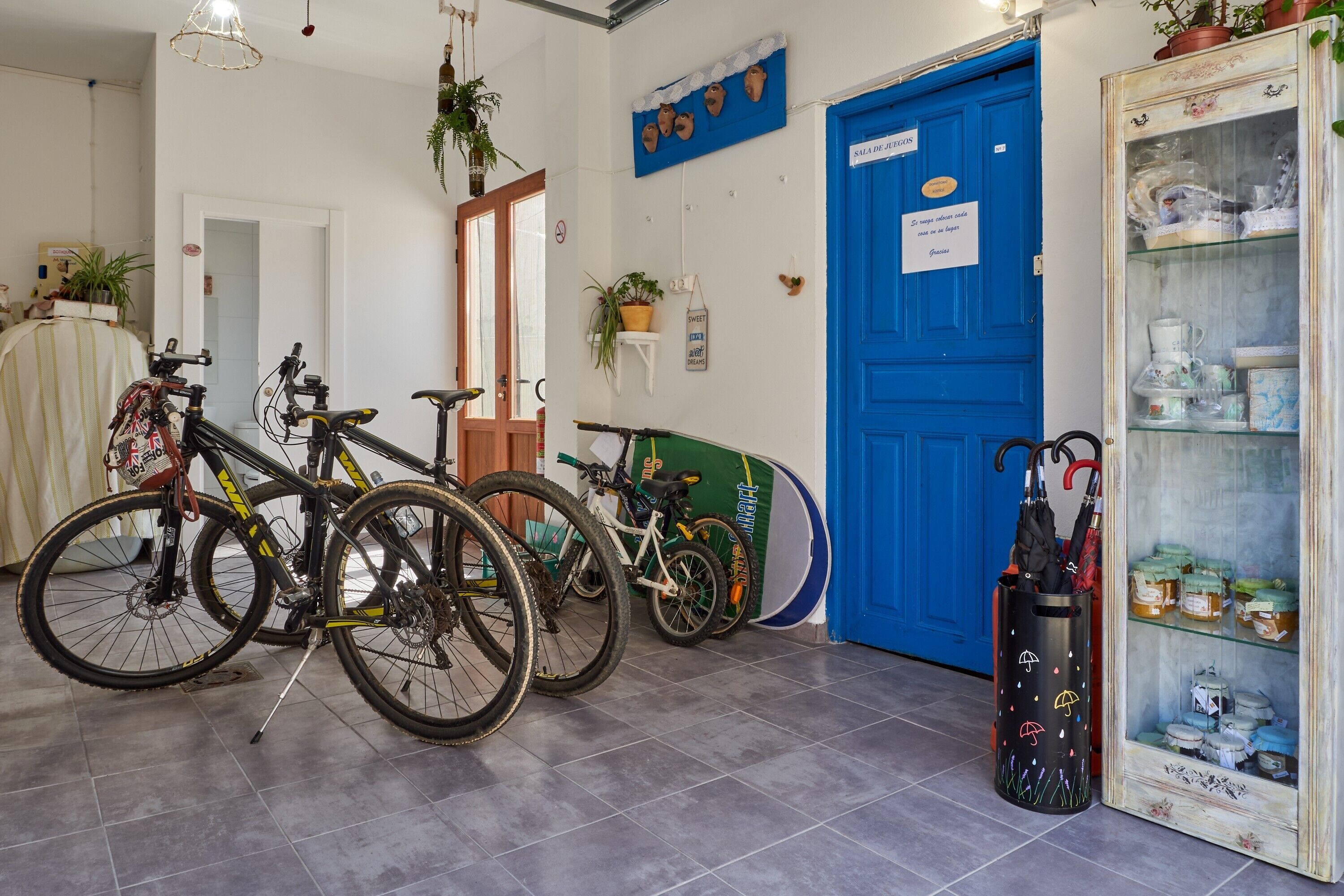 A room with bicycles, a blue door, a glass cabinet with items, and a wall-mounted sign.