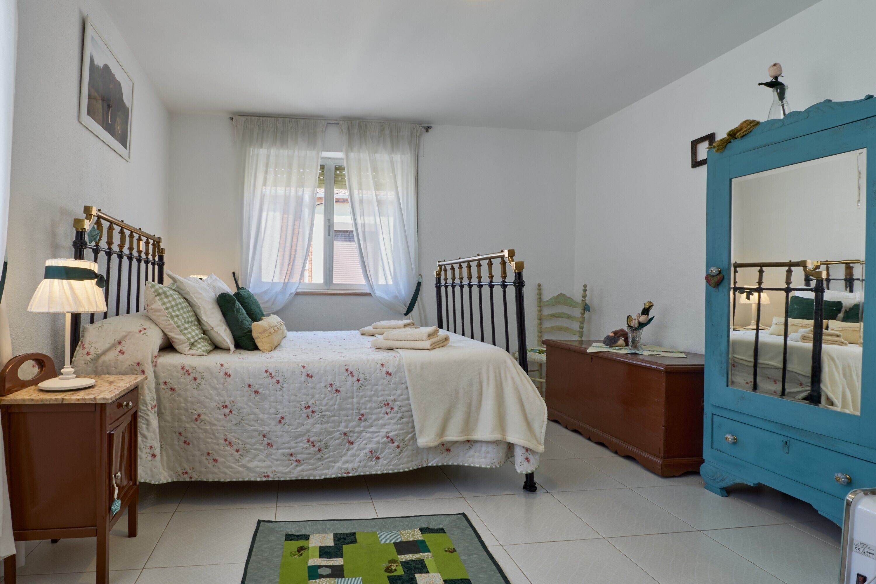 Een slaapkamer met een bed, een dressoir, een spiegel en een raam met gordijnen.