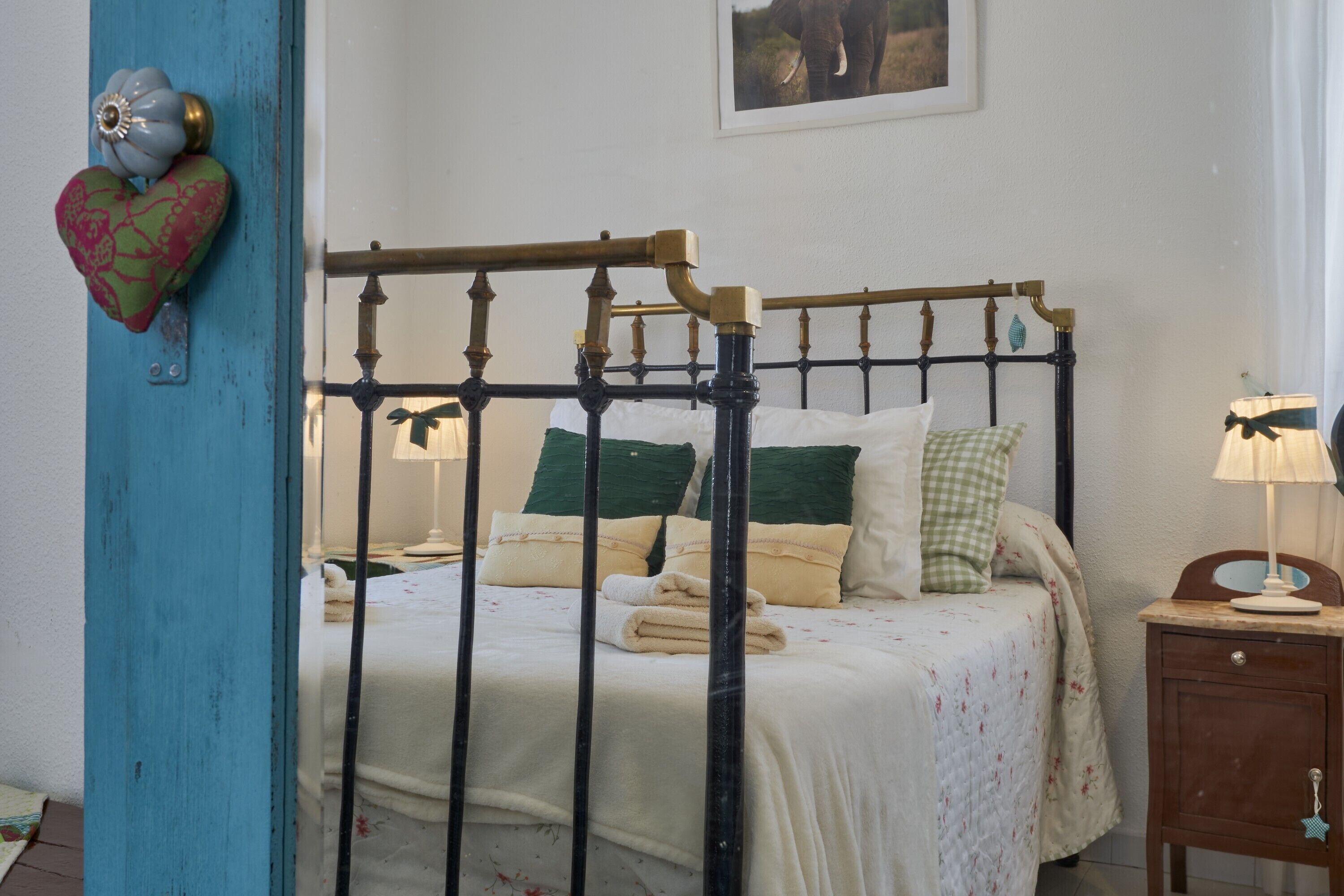 A bed with a metal frame, a bedside table with a lamp, and a wall-mounted heart-shaped decoration.