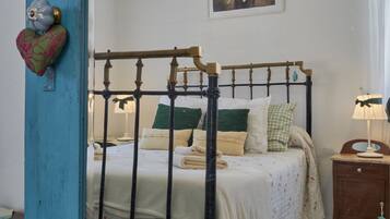 A bed with a metal frame, a bedside table with a lamp, and a wall-mounted heart-shaped decoration.