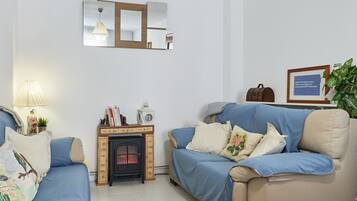 A living room with a sofa, a small table with a clock, a fireplace, and a mirror on the wall.