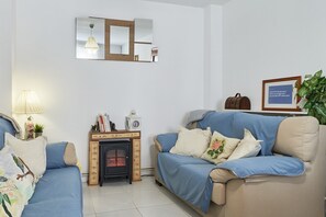 A living room with a sofa, a small table with a clock, a fireplace, and a mirror on the wall.
