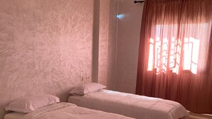 Two single beds with wooden frames in a room with textured walls and a large window with curtains. - Locanda Residence (Saâda)