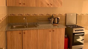 A kitchen with wooden cabinets, a granite countertop, a stainless steel sink, a coffee maker, a kettle, a gas stove, and a red gas cylinder. - Locanda Residence (Saâda)