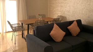 A living room with a sofa, two chairs, a dining table, and a vase with a flower. - Locanda Residence (Saâda)