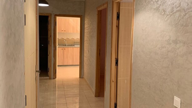 A hallway with a tiled floor leading to a kitchen area with wooden cabinets and a sink. - Locanda Residence (Saâda)