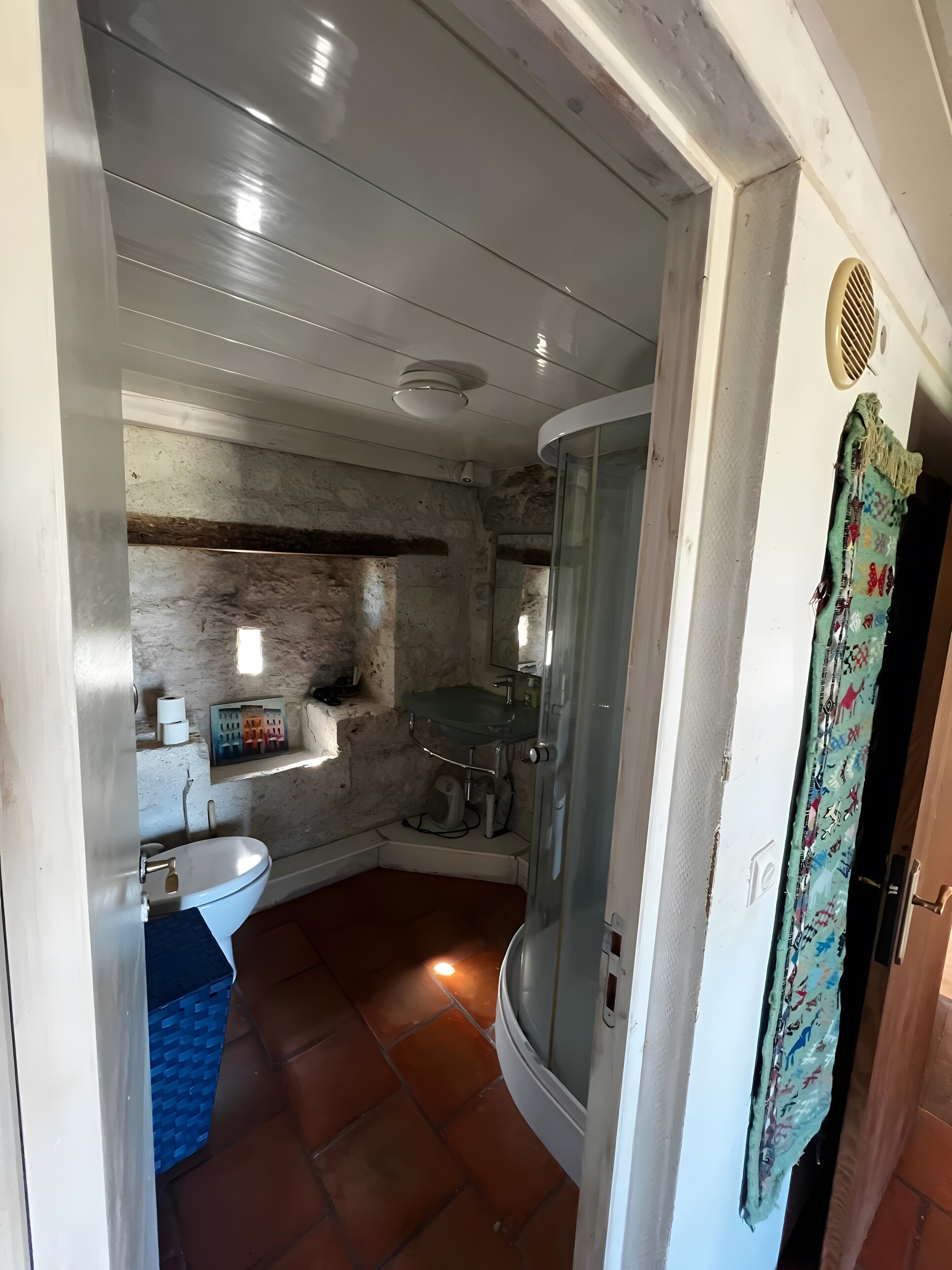 Une salle de bain avec un lavabo, des toilettes, une douche et un mur en pierre.