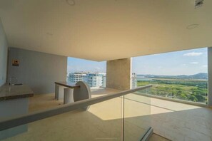 Un interior moderno con área de cocina, barandilla de vidrio y vistas a un paisaje urbano.