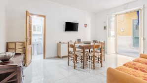 Una stanza con tavolo da pranzo, sedie, televisione, divano, angolo cottura e bagno.