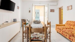 Una stanza con un tavolo da pranzo, sedie, un divano, una televisione e una porta che dà su un'altra stanza.