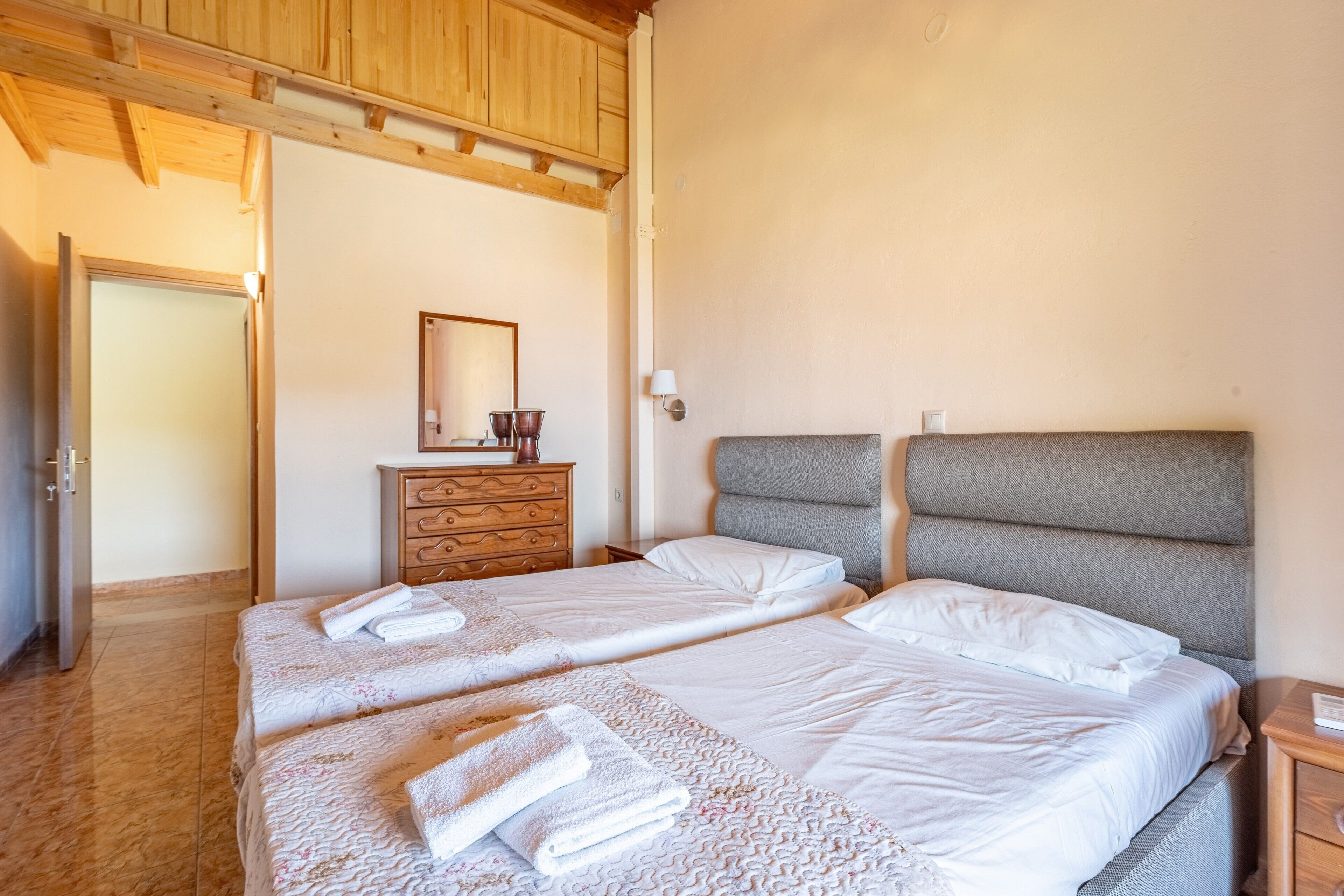 A room with two beds, a wooden dresser, a mirror, and a lamp.