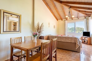 Une pièce comprenant une table à manger en bois, des chaises, un canapé, un téléviseur et une fenêtre donnant sur un beau paysage.