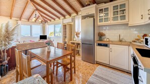Eine Küche mit Holzbalken, weißen Schränken, einem Edelstahlkühlschrank und einem Essbereich mit Tisch und Stühlen.