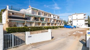 A multi-story hotel with balconies, a gated entrance, and a parking area. - Apartment 'Bella Mar' with Sea View, Private Terrace and Air Conditioning (L' ESCALA)