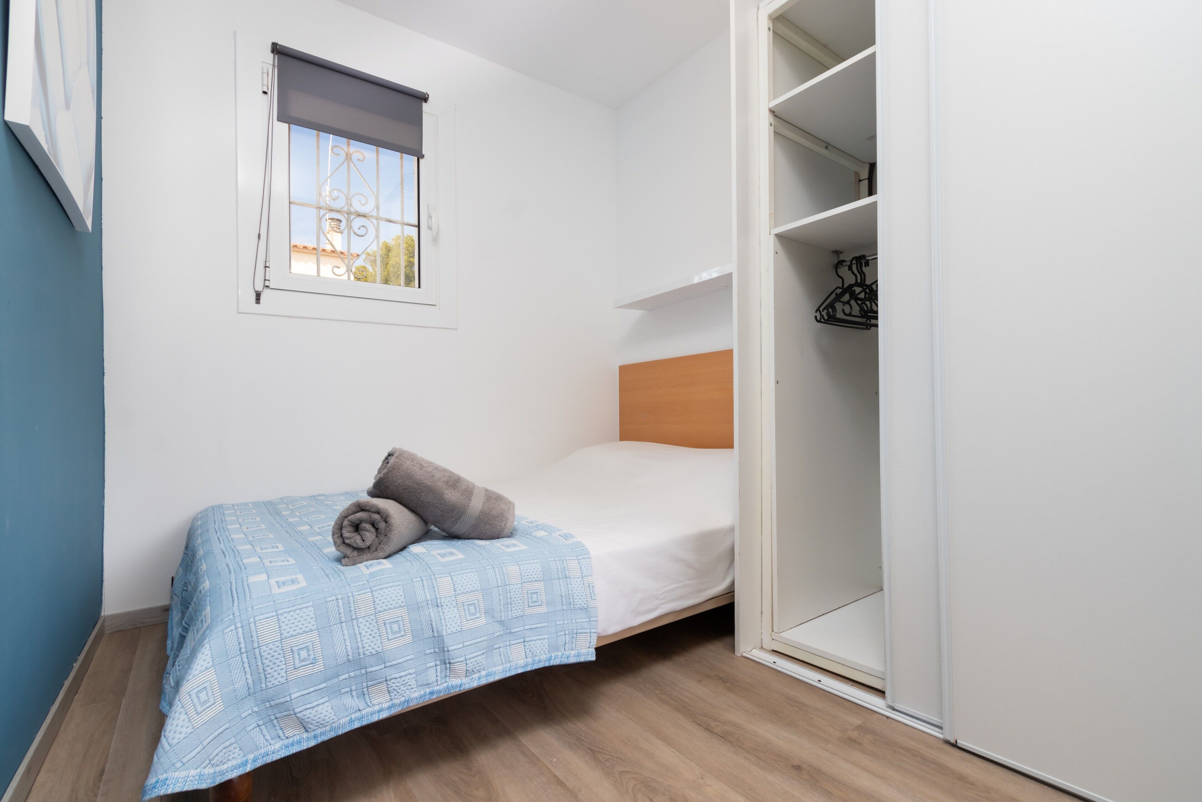 A small bedroom with a single bed, a window with a blind, and a wardrobe.