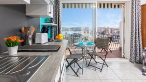 A balcony with a view of a cityscape, a small table with chairs, and a kitchen area with a sink and utensils. - Apartment 'Bella Mar' with Sea View, Private Terrace and Air Conditioning (L' ESCALA)
