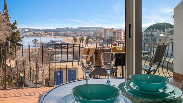 A balcony with a table set for two, overlooking a beach and cityscape. - Apartment 'Bella Mar' with Sea View, Private Terrace and Air Conditioning (L' ESCALA)
