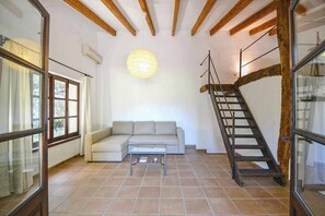 A living room with a sofa, a coffee table, a staircase, and a hanging light fixture. - Country House 'Sestadors' with Private Pool, Wi-Fi and Air Conditioning (Illes Balears)