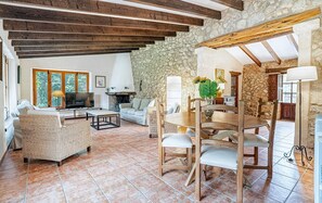 A spacious living area with a stone wall, wooden beams, a fireplace, and a dining set. - Country House 'Sestadors' with Private Pool, Wi-Fi and Air Conditioning (Illes Balears)