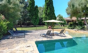 A swimming pool with lounge chairs and an umbrella, surrounded by a stone deck and greenery. - Country House 'Sestadors' with Private Pool, Wi-Fi and Air Conditioning (Illes Balears)