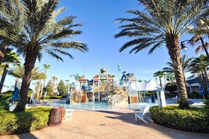 Een waterpark met een zwembad, palmbomen en een gebouw met een toren.