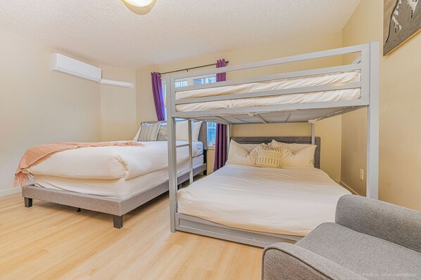 A room with two single beds and a bunk bed, wooden flooring, and a grey sofa.