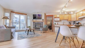 Una sala de estar moderna con chimenea, un comedor y una cocina con gabinetes de madera.