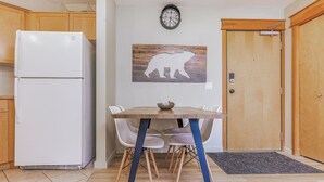 Una cocina funcional con refrigerador, una mesa de comedor con sillas, un reloj y una puerta de madera.