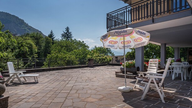 A patio with stone flooring, white chairs, an umbrella, and a view of a mountain.