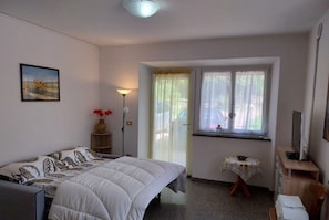 Un dormitorio con cama, mesita de noche, lámpara, ventana con cortinas y un cuadro en la pared.