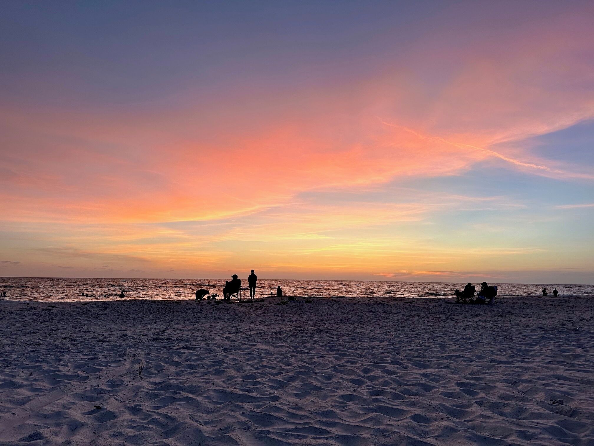 Ein Strand mit Menschen und einem Hund, der Himmel ist bunt.