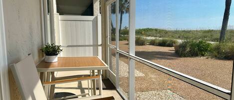 Un balcón con una mesa de madera, una silla, una planta en maceta y vistas a la playa y palmeras.