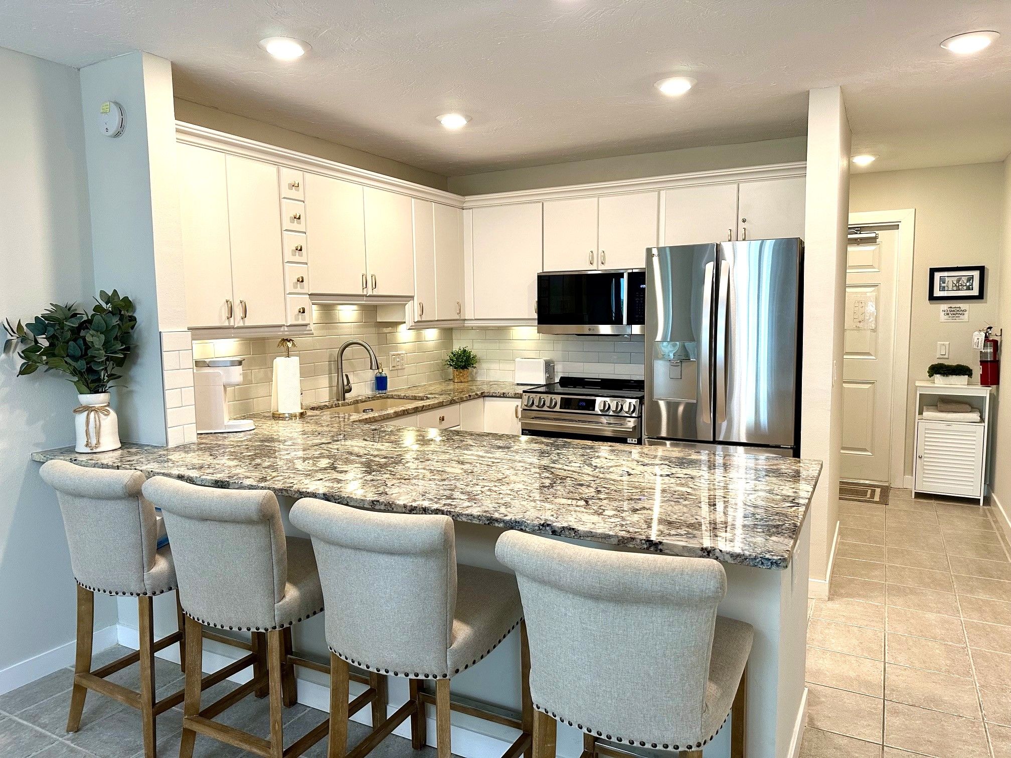 A modern kitchen with white cabinets, a stainless steel refrigerator, a microwave, and a granite countertop.
