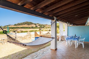 Un hamac sous un toit en bois, une piscine, une table avec des chaises et une vue sur les collines.