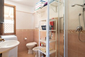 Une salle de bain équipée d’un lavabo, de toilettes, d’une douche et d’étagères où sont rangées les serviettes.