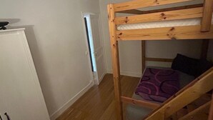 A compact room with a bunk bed, a white wardrobe, and a door leading to another room.