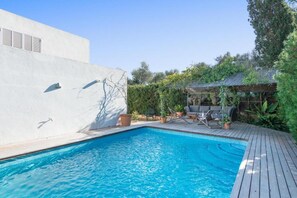 A swimming pool with a wooden deck, surrounded by potted plants and a white wall. - Villa 'Es Tancat' with Sea View, Private Pool and Wi-Fi (Sa Ràpita)